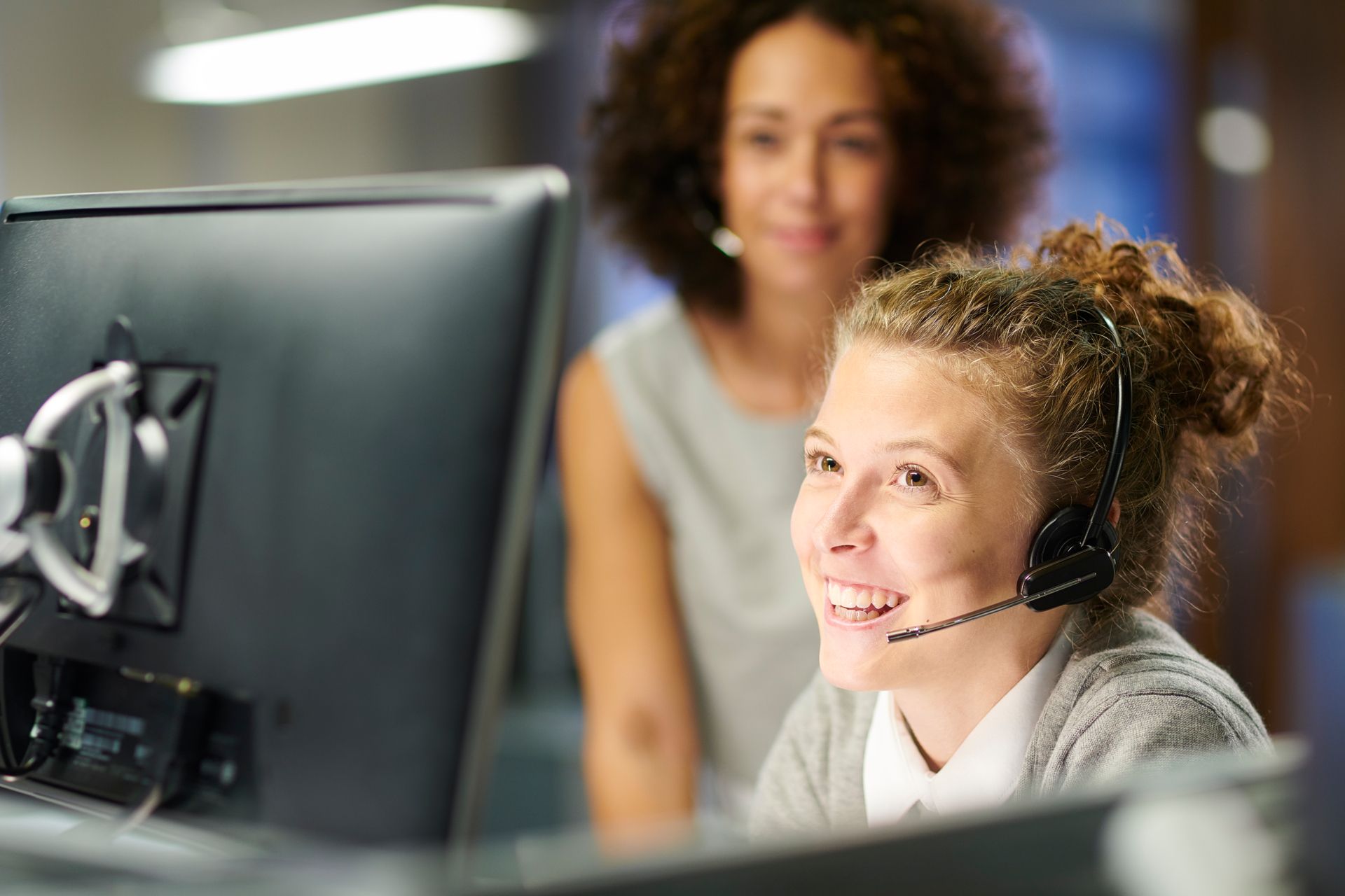 Frau mit Headset lächelt, während sie an einem Computer in einem Büro arbeitet.