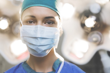 Frau in OP-Kleidung und mit chirurgischer Maske in einem Raum.