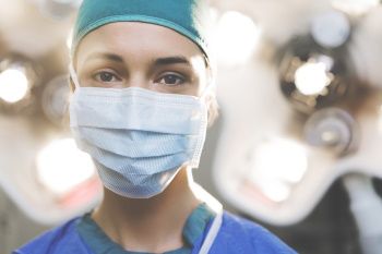 Frau in OP-Kleidung und mit chirurgischer Maske in einem Raum.